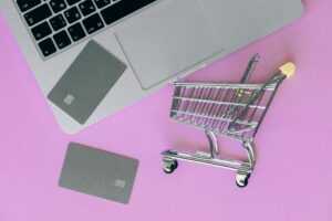 A minimalist flat lay of a credit card, laptop, and miniature shopping cart.